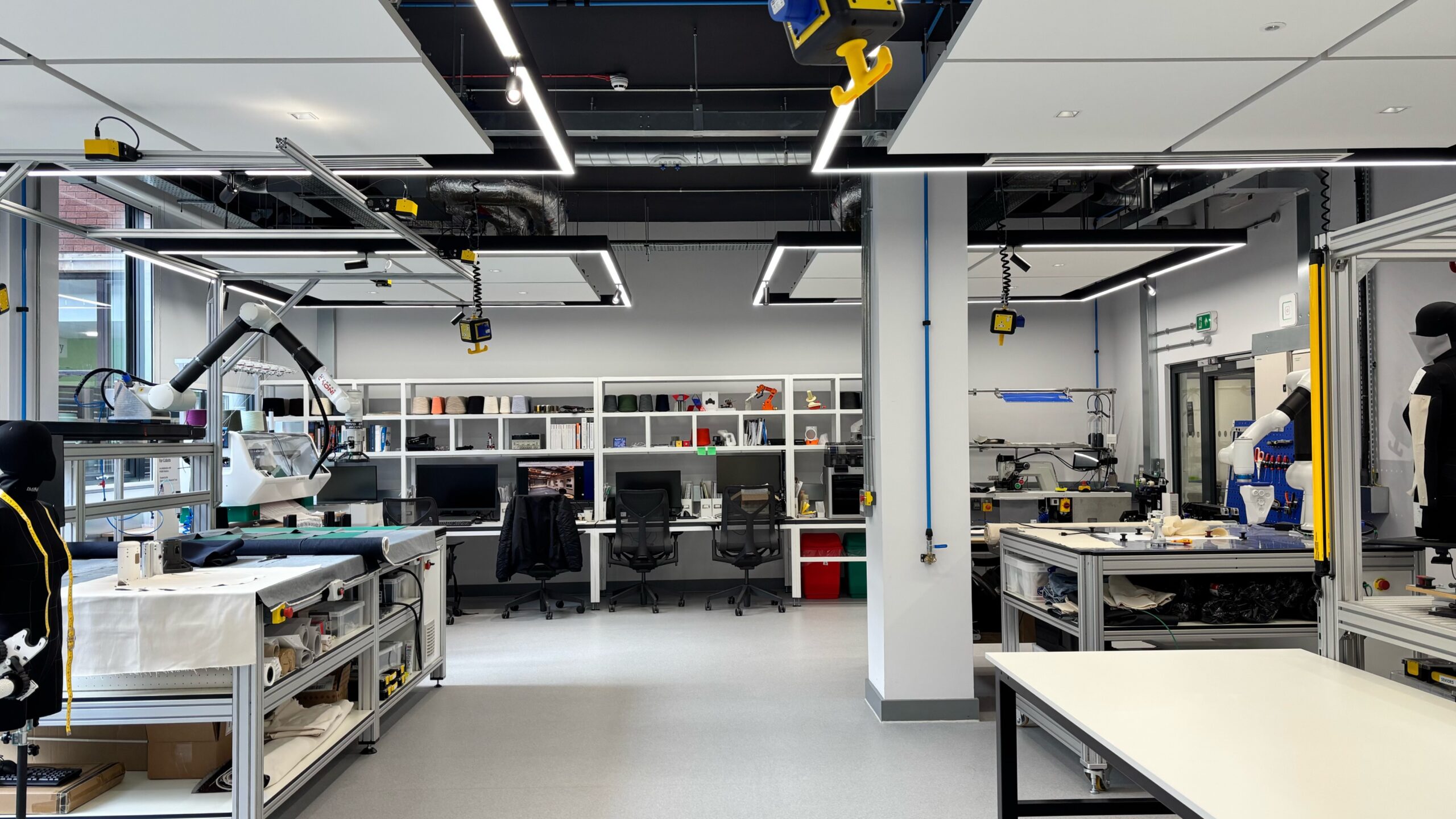 a wide angled shot of the Robotics Living Lab, showing different robotic workstations, desks as well as knit and sewing machines 